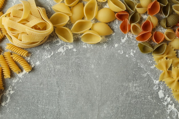 Uncooked pasta and flour on gray textured