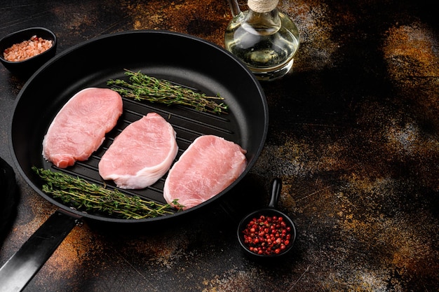 Uncooked pork chop set, on frying cast iron pan, on old dark rustic table background, with copy space for text