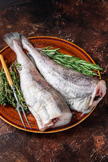 Uncooked Raw cod or codfish fish in rustic plate with herbs and fork.   Top view.