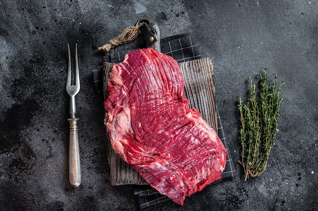 Uncooked Raw Flank or flap beef steak on butcher board. Black background. Top view.