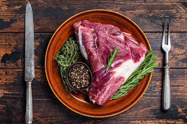 Uncooked Raw goat thigh or leg with rosemary and thyme in rustic plate