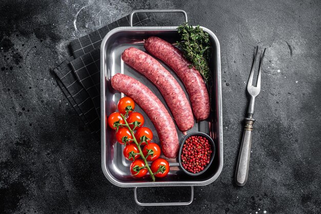 Uncooked Raw lamb and beef meat sausages in kitchen tray with herbs Black background Top view