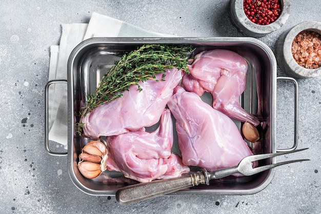 Uncooked Raw rabbit legs slices in a butcher tray with herbs. Gray background. Top view.