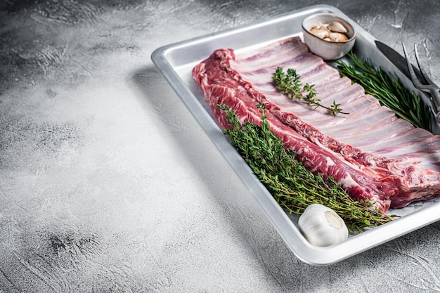 Photo uncooked raw rack of lamb ribs in baking dish with herbs. white background. top view. copy space.