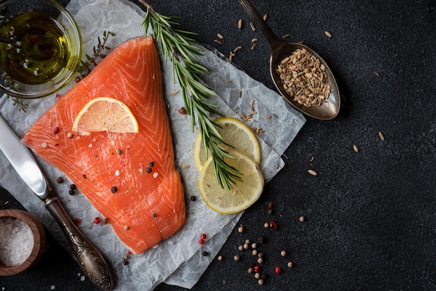 Uncooked raw salmon fish with herbs on dark background