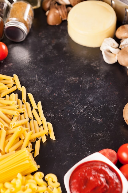 Uncooked raw spachetti and pasta next to different products on vintage dark background