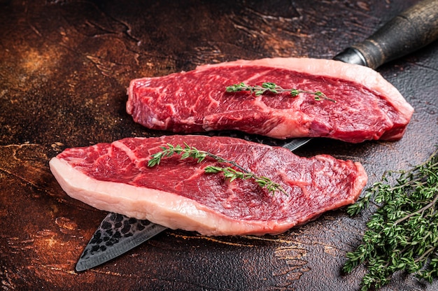 Uncooked Raw top sirloin cap or rump beef meat steaks on a butcher knife. Dark background. Top view.