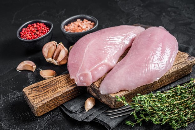 Uncooked Raw Turkey Breasts fillet steaks with herbs. Black background. Top view.