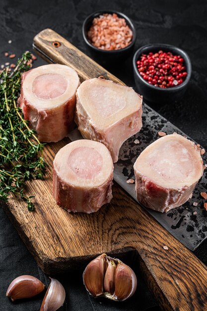 Uncooked Raw veal Marrow bones on butcher board with meat cleaver. Black background. Top view.