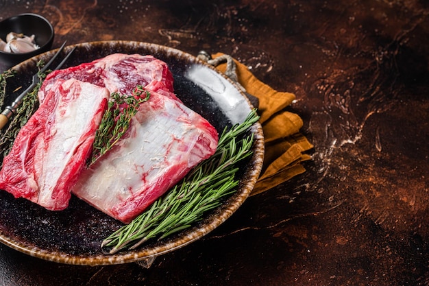 Uncooked Raw veal Short Ribs on rustic plate with rosemary. Dark background. Top view. Copy space.