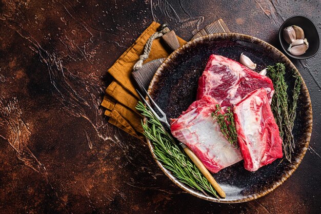 Uncooked raw veal short ribs on rustic plate with rosemary dark\
background top view copy space