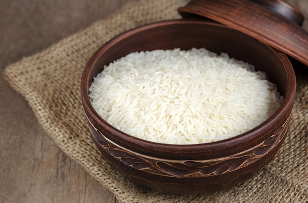 Photo uncooked rice in a clay bowl on wooden background