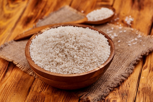 Uncooked rice in a wooden bowl with the wooden spoon full of rice, rustic background. Close up.