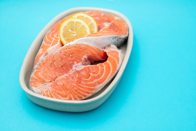 Uncooked salmon with lemon on dish on blue background