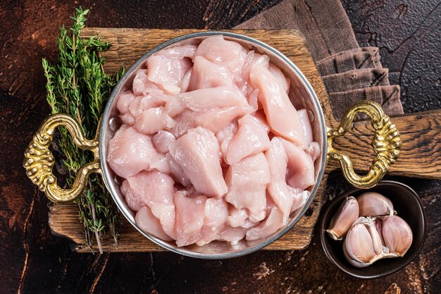 Uncooked sliced poultry meat, Raw Diced chicken breast fillets in rustic skillet. Dark background. Top view.