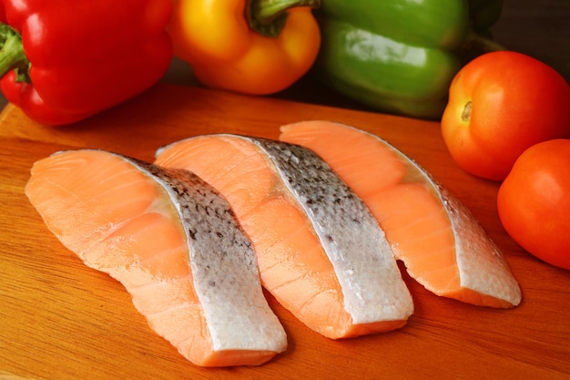 Uncooked sliced salmons on a cutting board surrounded with colorful fresh vegetables
