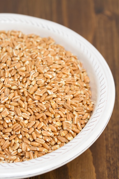 Uncooked spelt on white plate on wooden surface