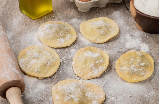 Uncooked stuffed raviolonis or raviolis with flour over wooden table