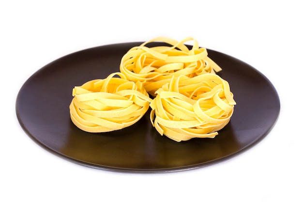 Uncooked tagliatelle on a black ceramic plate. Isolated