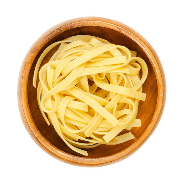 Uncooked tagliatelle pasta in a wooden bowl