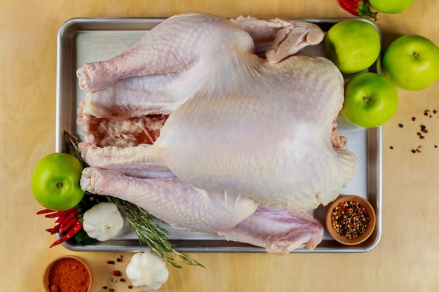 Uncooked turkey with cooking ingredients and spices on wooden surface.