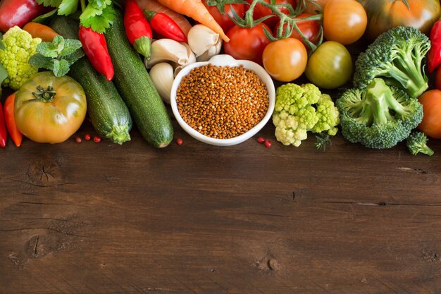 Uncookes brown millet in a bowl with vegetables on wood