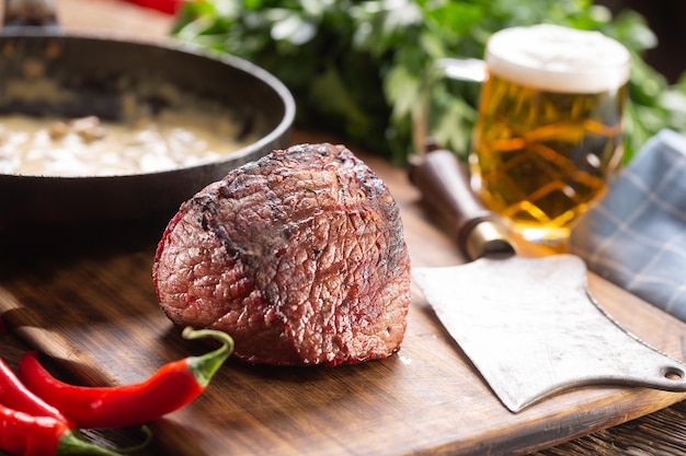 Unctut stuk pan-aangebraden rumpsteak op een snijplank met verse pepers en een biertje.