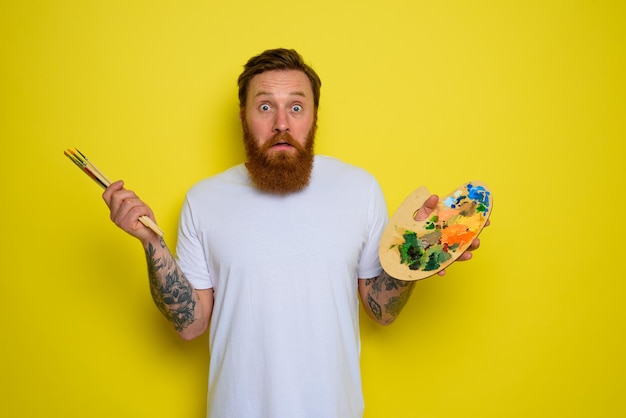 undecided man with beard and tattoo is ready to draw with brushes