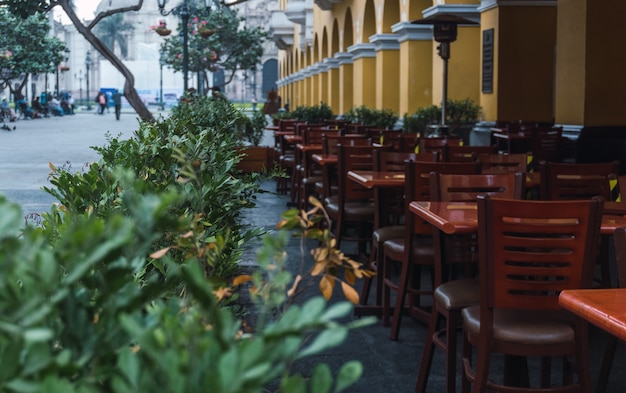 Underexposed outdoor restaurant tables in historic center of Lima Peru, flowerpot around wooden tables, yellow columns