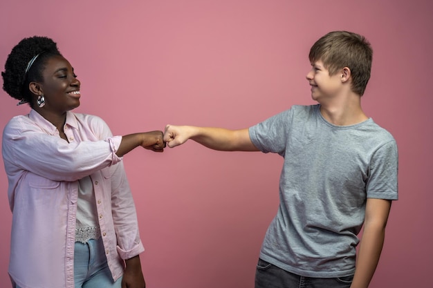 Понимание. Улыбающийся парень с синдромом дауна и африканская американка, стоящая напротив, трогают кулаком и смотрят друг на друга