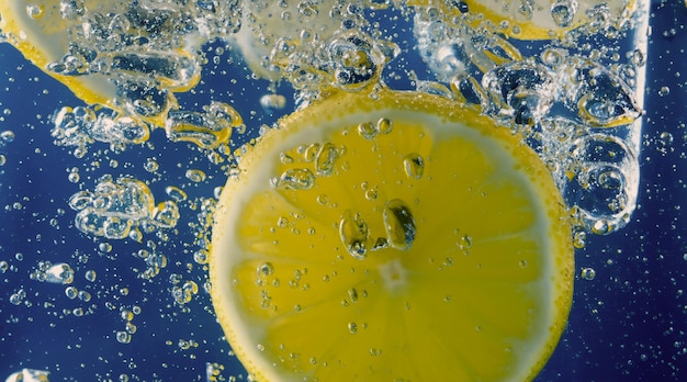 Underwater lemon slice in soda water or lemonade with bubbles Refreshing soda tonic fizzy cocktail Close up of lemons and ice cubes in glass Lime in splashing sparkling water cold drink beverage