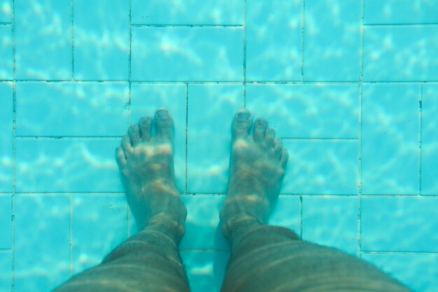 Underwater photo, bottom of swimming pool with blue tiles, man legs standing on it.