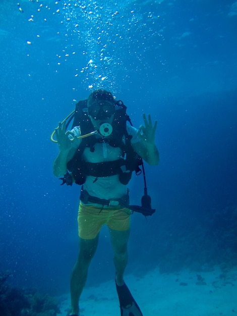 Underwater shoot of a man diving with scuba, looking at the camera and showing ok signal