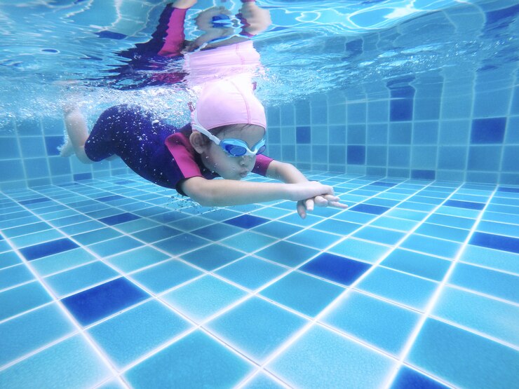 水中の若いかわいい女の子は彼女の水泳の先生と一緒にスイミングプールで泳いでいます。