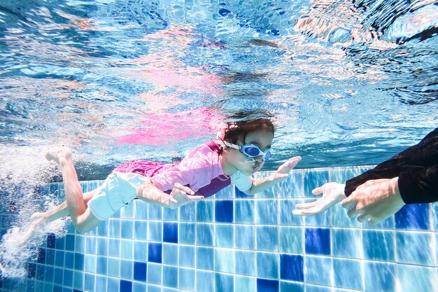 Underwater young little cute girl is swimming in the swimming pool with her swimming teacher.