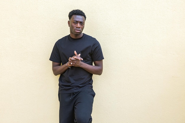 Photo unemotional young black guy standing near wall on street