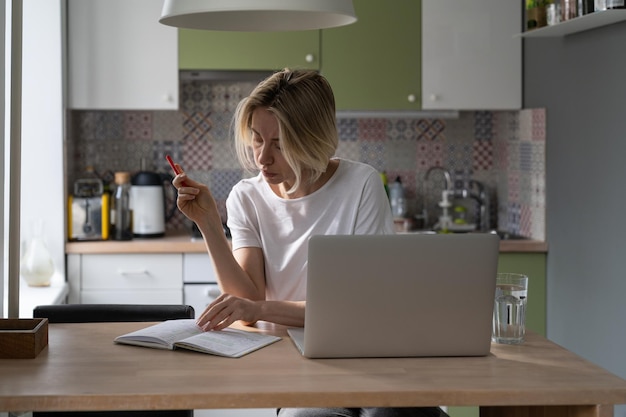 Unemployed woman reads notebook writing list of contacts looking for vacancies on laptop on table