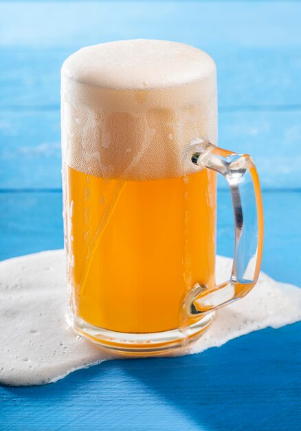 Unfiltered beer in a pint with spilled foam on a blue table close-up of a pint of german wheat beer