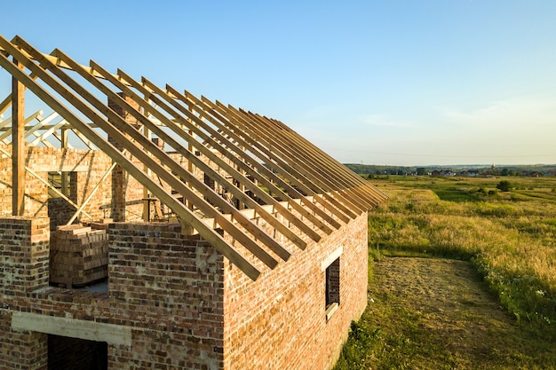 Unfinished brick house with wooden roof structure under construction.