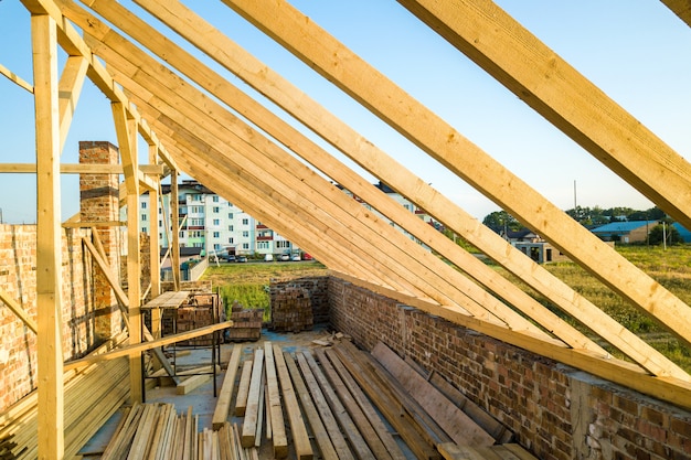 Unfinished brick house with wooden roof structure under construction.