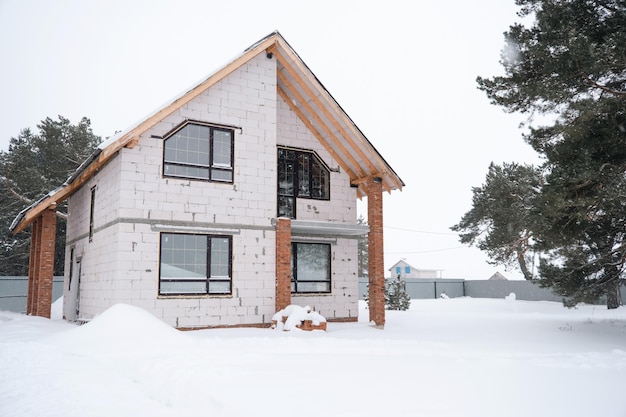 Costruzione incompiuta una casa fatta di blocchi porosi in sospensione invernale durante la stagione di costruzione ghiacciata neve e facciata della casa senza decorazione esterna con finestre trapezoidali