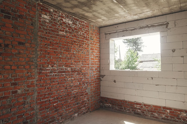 Unfinished house inside Aerated concrete blocks and brick walls with windows doorways and concrete floor Process of house building at construction site New house construction