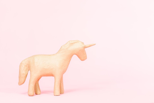 Unfinished paper mache figurine of unicorn on a pink background.