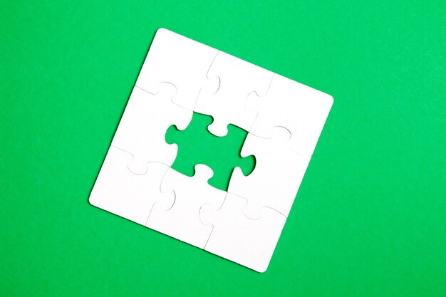 Unfinished puzzle made of white cardboard on a green background and one unsuitable part from another puzzle, one piece is missing, copy space
