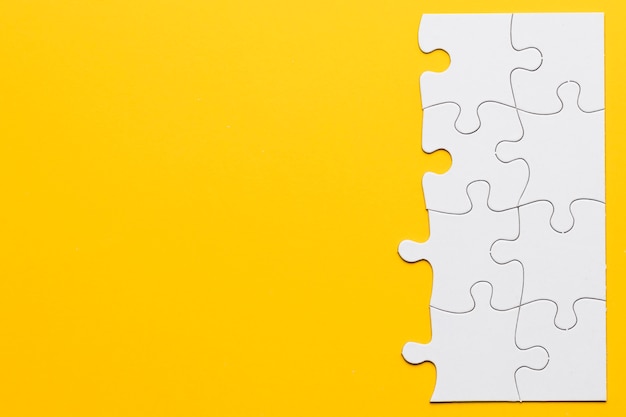 Unfinished white jigsaw puzzle pieces on yellow background