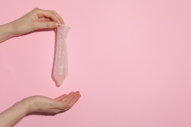 Unfolded condom in hand on pink background place for text