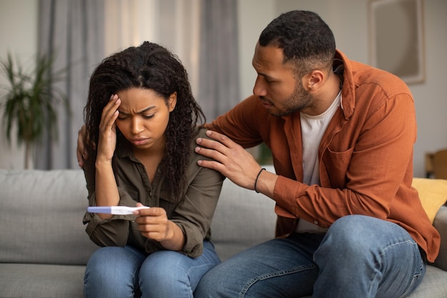 Unhappy African American Couple Holding Negative Pregnancy Test At Home