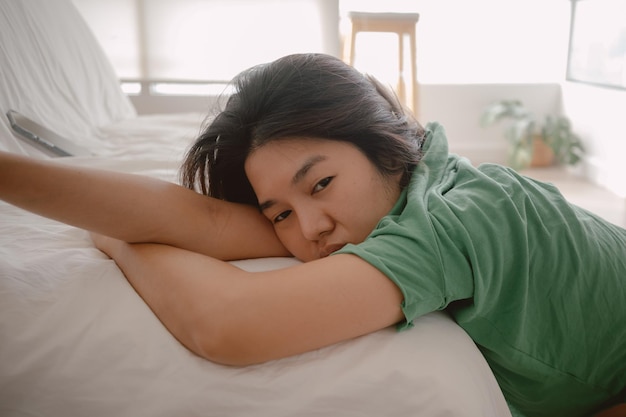 Unhappy asian thai woman leaning on white cough sofa while resting head on arm with sadness sitting