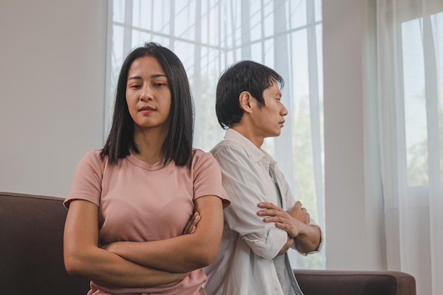 Unhappy asian young couple fights on couch, relationship is in trouble. Different people are angry and use emotions at each other. Wife has an expression of disappointment and upset with her husband.