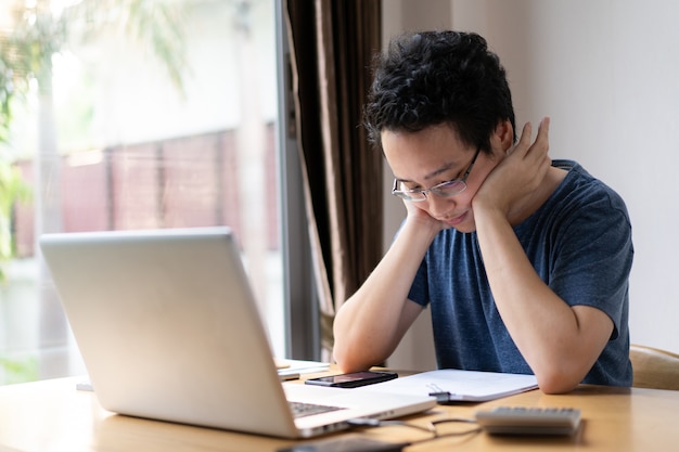 Unhappy asian young man working at his home portrait.\
uncomfortable working space is not good for employee. stressful\
asian man.